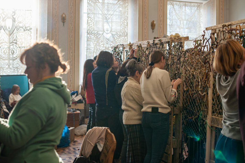 A group of women indoors creating camouflage nets, emphasizing community support and collaboration.