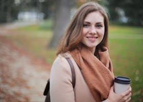 Portrait of a smiling woman holding a coffee cup in a serene autumn park setting.